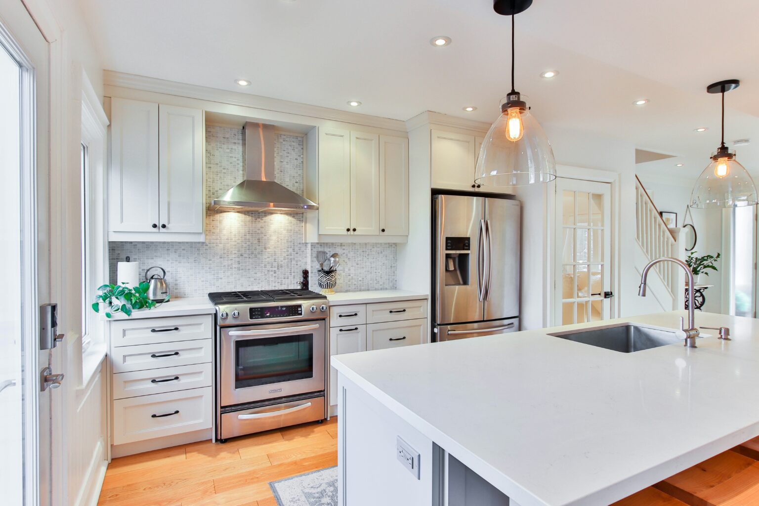 Modern kitchen interior featuring stainless steel appliances, including a gas stove and refrigerator, with white cabinetry, a large island, and pendant lighting, relevant to plumbing services and home renovations in Nottingham.